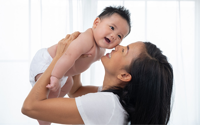 Laughing mother lifting her adorable newborn baby son in air