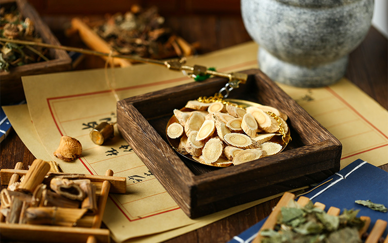 TCM physician weighing astragalus root slices on traditional scale.