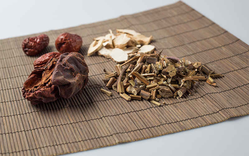 Assorted TCM herbs, including dried fruit and root pieces on mat.
