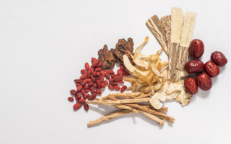 Assorted traditional Chinese medicinal herbs including goji berries, red dates, and sliced roots on white surface.