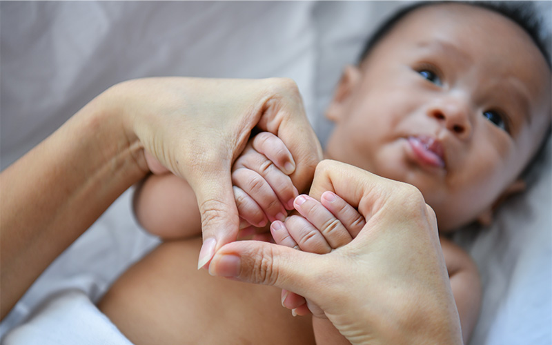 Close-up of adult gently holding baby’s hands in a heart shape on a white surface.