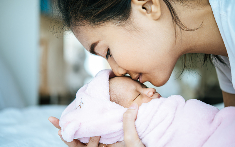 Mother kissing her baby to bond during postpartum care.