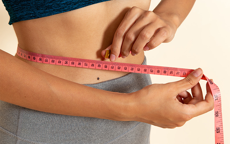 Person measuring waist with pink tape.