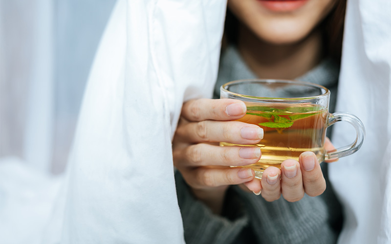 Person holding a warm cup of herbal tea wrapped in a blanket.