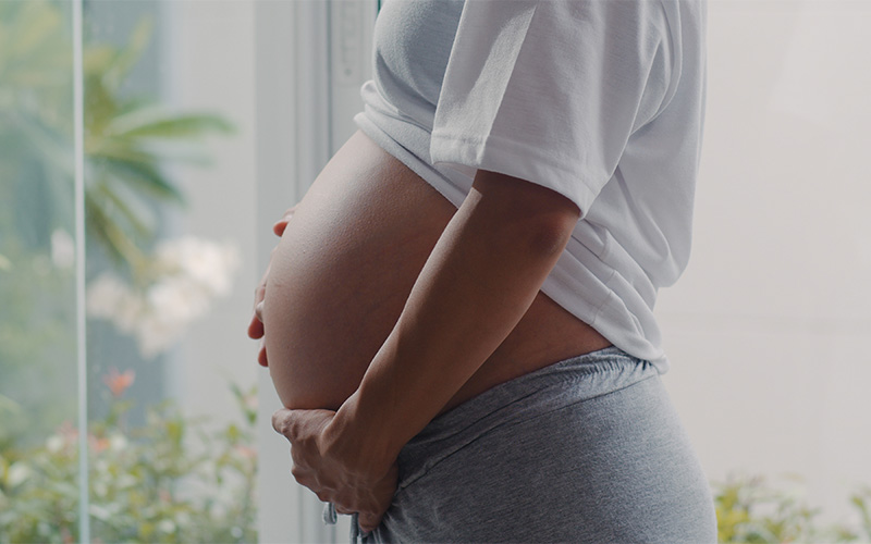 Pregnant woman holding belly, showing menstrual cycle fertility links.